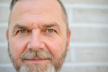 Sakallı, orta yaşlı bir adamın kameraya bakarken çekilmiş resmi.