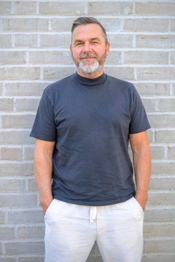 Son sınıf öğrencisi poz veriyor. Tuğla duvarın önünde gülümsüyor.