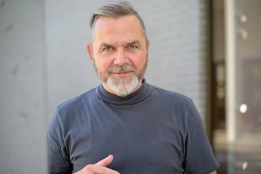 Sakallı kıdemli adam kameraya dikkatlice bakıyor ve içeride ciddi bir yüz ifadesi var.