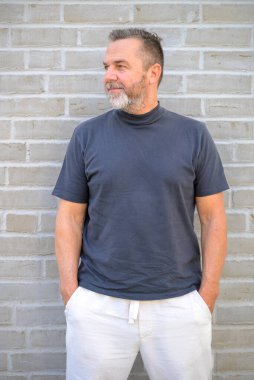 Son sınıf öğrencisi, tuğla duvarın önünde gülümseyen bir gülümsemeyle yan yan bakıyor.