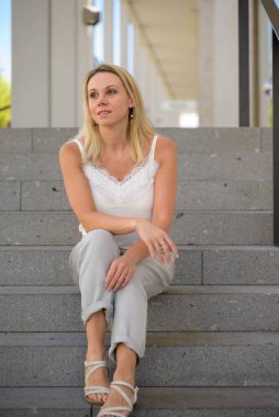 Pensive blond woman sitting on outdoor steps looking aside with an expression of longing