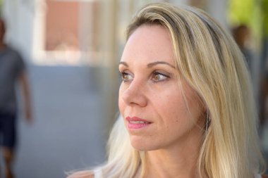 Thoughtful blond woman in a close up profile portrait looking off to the side with a pensive expression