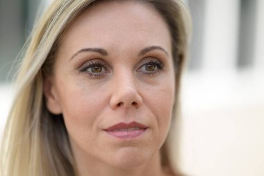 Close up head shot of an attractive blond woman looking away with a quiet smile outdoors