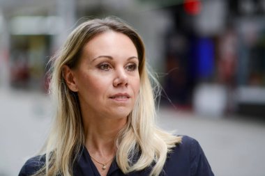 Çekici, orta yaşlı, mavi ceketli, hafifçe gülümseyen bir sarışının yan görünüşü. Alışveriş merkezindeki arka planda alışveriş yaparken.