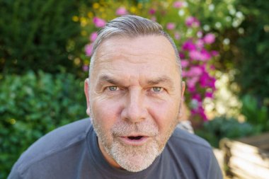 Orta yaşlı bir adam kameraya dikkatle bakıyor ve ciddi bir ifadeyle öne doğru eğiliyor.