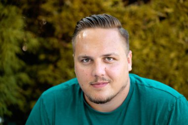 Genç adam kameraya dikkatlice bakıyor. Sonbaharda açık havada düşünceli bir gülümsemeyle.