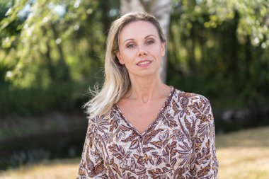 Olgun bir kadının başı ve omuzları kırsal alanda şehvetli bir gülümsemeye sahip.