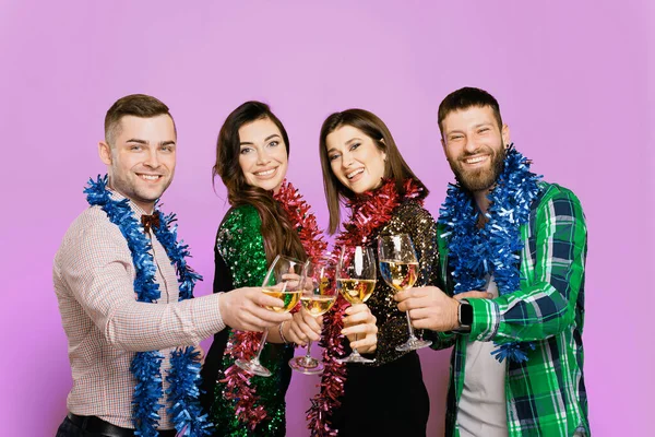 Two men and two girls 25s with New Year's rain on their shoulders clink glasses of white wine or champagne against a lilac background. Four friends with glasses of wine. New Year's party of friends.