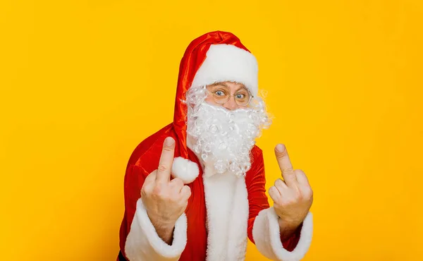 Santa claus shows middle fingers and looks at the camera on a yellow isolated background with copy space. Bad santa
