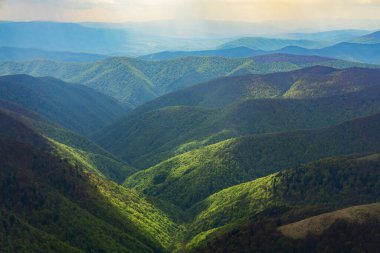 Güneş bulutlu gökyüzünün altında yeşil dağları aydınlattı.