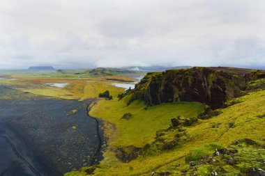 Güney İzlanda, Vik. Uçurumlar, yeşil vadi ve Dyrholaey yarımadasındaki siyah kumsal manzarası. Boşluk arkaplanı kopyala.