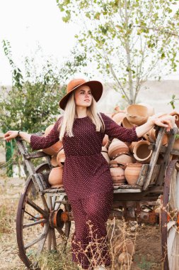 Ahşap kırsal araba dolusu çömlek sürahisinin yanında şapka ve elbise giyen genç bir kadın. Yavaş yaşam tarzı konsepti. Kapadokya Seyahat Maceraları.