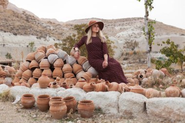 Dışarıda kilden tencerelerin yanında şapka ve elbise giyen genç bir kadın. Yavaş yaşam tarzı konsepti. Kapadokya Seyahat Maceraları.