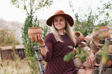 Şapka ve elbise giyen genç bir kadın ahşap kırsal yük arabasından çömlek sürahisi alıyor. Yavaş yaşam tarzı konsepti. Kapadokya Seyahat Maceraları.