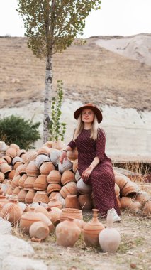 Dışarıda kilden tencerelerin yanında şapka ve elbise giyen genç bir kadın. Yavaş yaşam tarzı konsepti. Kapadokya Seyahat Maceraları.