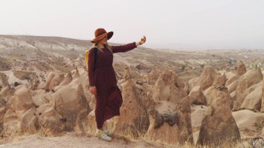 Kahverengi şapkalı ve uzun elbiseli gezgin bir kadın çöl vadisinde ve kayalarda yürüyor. Seyahat ve seyahat tutkusu konsepti. Kapadokya, Türkiye.