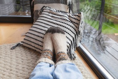 El yapımı halı ve yastıklarda örülmüş çoraplar ve mavi kot pantolon giyen kadın ayakları. Rahatlatıcı hygge konsepti. 