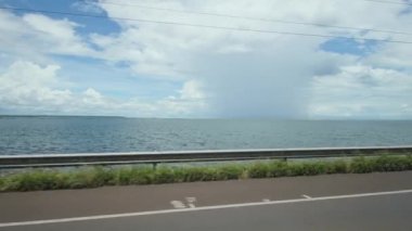 Driving on the riverside road on a sunny day but with rain falling far in the background. Landscape of Helio Serejo bridge, border bridge with the state of Mato Grosso do Sul and Sao Paulo, Brazil.