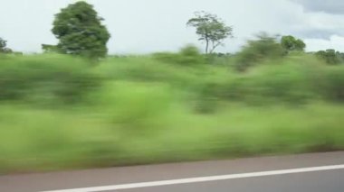 View from the side window of a car during a road trip, landscape of green vegetation and rural areas on the background.