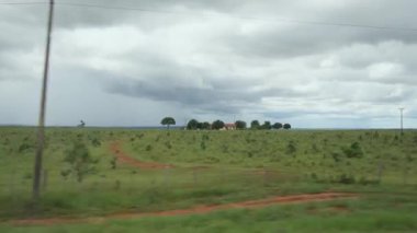 View from the side window of a car driving on the road passing by landscapes of rural areas on a cloudy day with no rain, but raining distantly. Landscape of Mato Grosso do Sul state, Brazil.