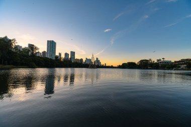 Gün batımında Igapo Gölü, Londrina - PR, Brezilya. Ağaçlarla çevrili güzel şehir gölü, sakin su ve arka plandaki şehir binaları..