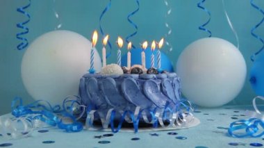 Mavi arka planda mumları ve hava balonları ve süslemeleri olan lacivert doğum günü pastası.
