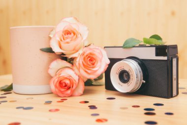 Old photo camera with roses flowers and pink cup of tea or coffee, beautiful vintage card