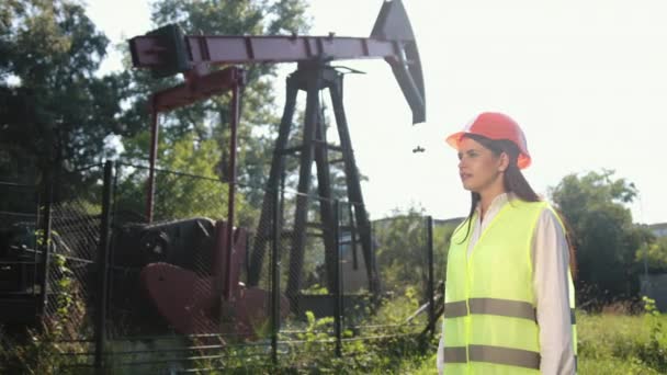Kvinnlig arbetare i oljefält talar i telefon bär orange hjälm, arbetskläder — Stockvideo