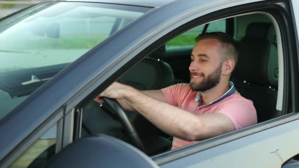Młody człowiek z brodą, dotyka kierownicy rękami, pociągnięciami, uśmiechem — Wideo stockowe