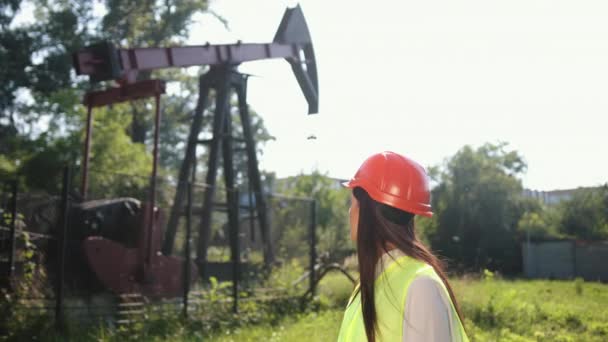 Female worker in oil field talking on phone wearing orange helmet, work clothes — Stock Video