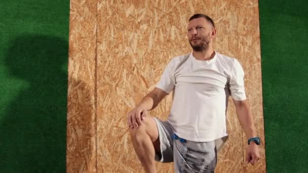 Egy tréningruhás férfi térden állva tartja a lábát, hogy megnyújtsa az ínszalagokat. Sport — Stock videók