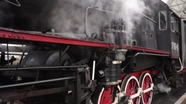 Retro buhar treni tren istasyonundan ayrılıyor. Mavi arabalı eski siyah buhar treni