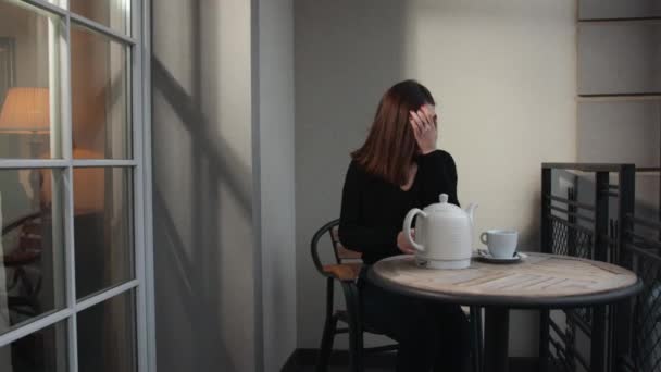 Νεαρή όμορφη γυναίκα κάθεται σπίτι στην καρέκλα από το παράθυρο με φλιτζάνι ζεστό καφέ — Αρχείο Βίντεο