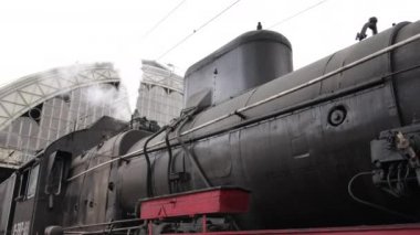 Retro buhar treni tren istasyonundan ayrılıyor. Mavi arabalı eski siyah buhar treni