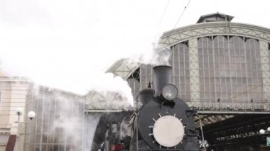 Retro buhar treni tren istasyonundan ayrılıyor. Mavi arabalı eski siyah buhar treni