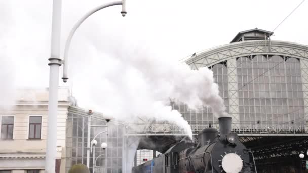 レトロな蒸気機関車が駅から出発する。青い車と古い黒い蒸気機関車 — ストック動画