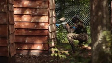 Paintball sport player wearing protective mask aiming gun from shelter