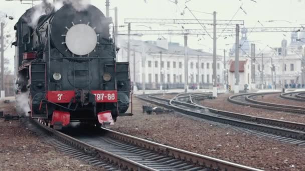 Pociąg lokomotywa parowa zbliża się do stacji przejeżdżającej przez podwórko towarowe — Wideo stockowe