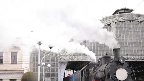 レトロな蒸気機関車が駅から出発する。青い車と古い黒い蒸気機関車 — ストック動画