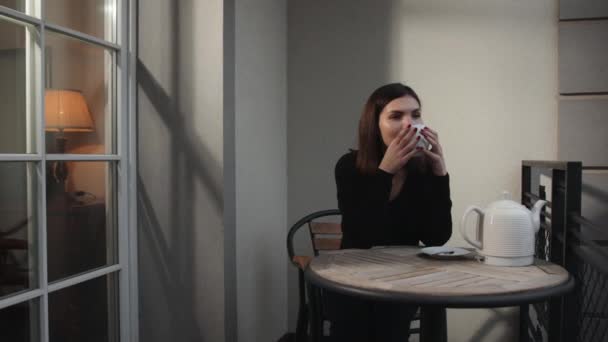 Női modell kezében csésze kávét. Álmodozó szőke nő ül az erkélyen. — Stock videók