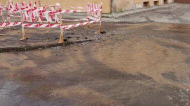 Trafik konilerinin yanında yol suyu fışkırır. Su birikintisi asfalta zarar veriyor. Kanalizasyon