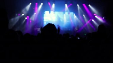 Parlak sahne ışıkları önünde konser kalabalığı siluetleri. İnsanların silueti
