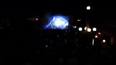 Parlak sahne ışıkları önünde konser kalabalığı siluetleri. İnsanların silueti
