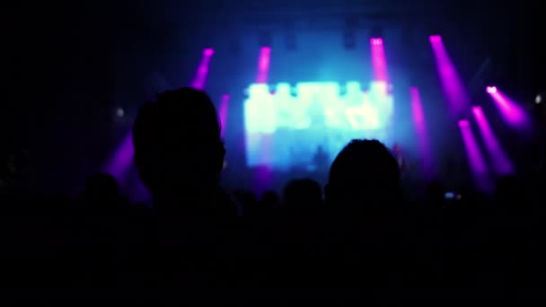 Aydınlatılmış sahne ışıkları. Kaldırılan eller görülebilir. Konser kalabalığı siluetleri — Stok video