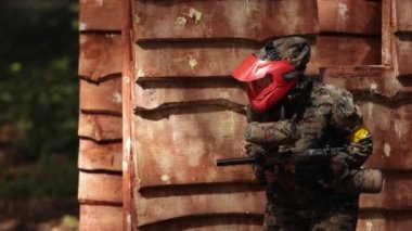 Koruyucu maske takan paintball oyuncusu saldırı altında silah barınağını hedefliyor
