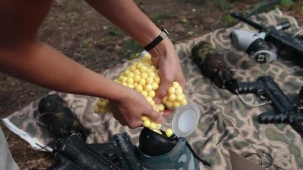 Le mani degli uomini versano palle di paintball gialle nel serbatoio dell'arma. Preparazione per il gioco — Video Stock