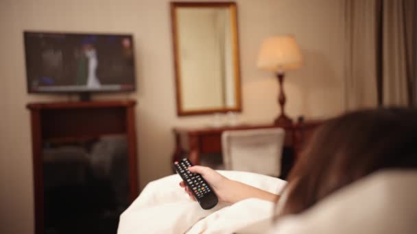 Películas en casa en servicios de streaming, control remoto de televisión está en una mano femenina — Vídeos de Stock