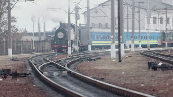 Parní lokomotiva přijíždí stanicí projíždějící skladištěm zboží — Stock video