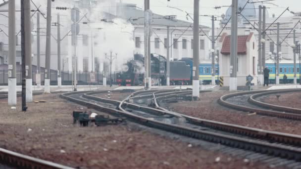 Паровой паровоз приближается к станции, проходящей через товарный двор — стоковое видео