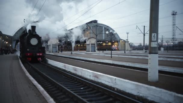 Parní lokomotiva přijíždí stanicí projíždějící skladištěm zboží — Stock video